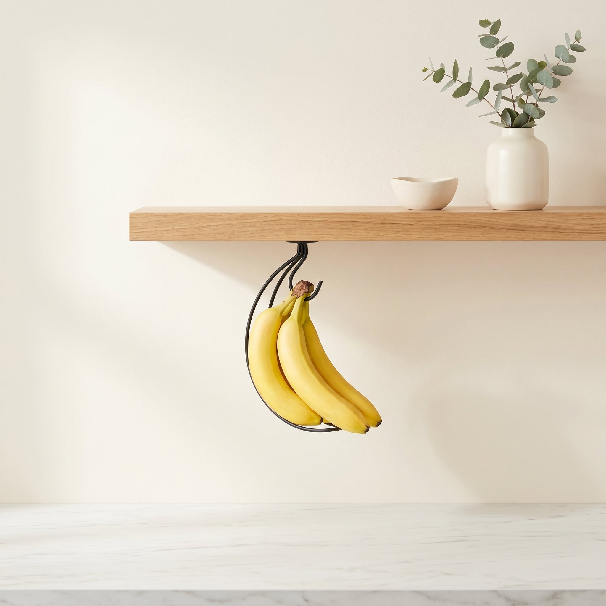 Under-cabinet banana hook mounted beneath a wooden floating shelf